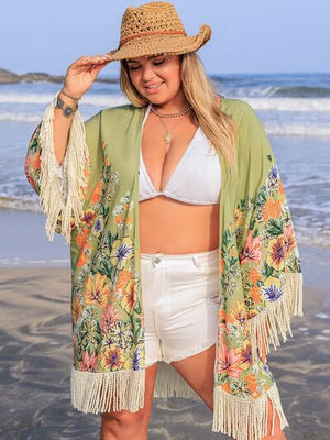 Model in a floral fringe cover-up over a swimsuit, enjoying a sunny beach day with a straw hat.