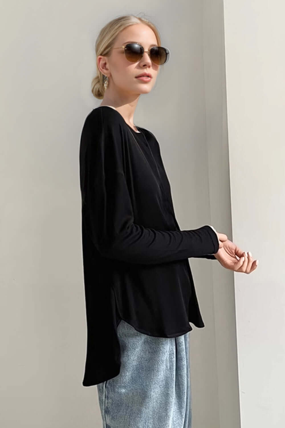 Stylish woman wears black high-low long sleeve t-shirt with slight stretch, paired with sunglasses for a chic monochrome look.