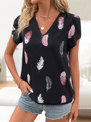 Woman wearing a printed V-neck short sleeve blouse with feather design, paired with denim shorts.