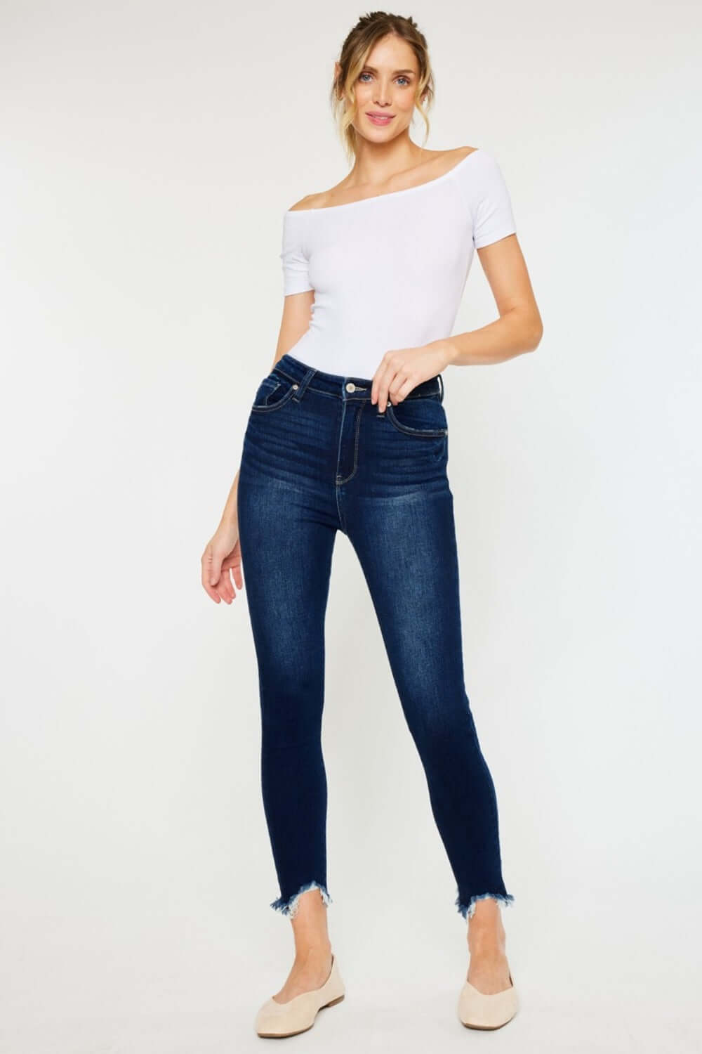 Woman wearing high rise frayed ankle skinny jeans with a white off-the-shoulder top and beige flats