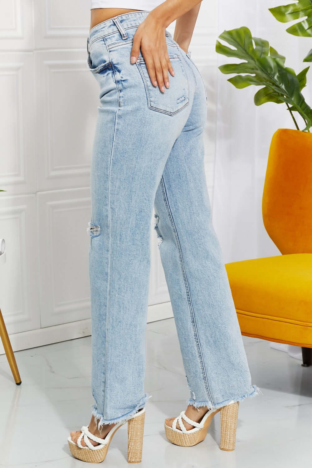 Woman wearing high-waist light wash distressed 90's dad jeans with raw hem standing in stylish room