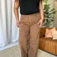 Woman modeling high-rise garment dye wide leg jeans in a brown color, paired with a black top and white sneakers.