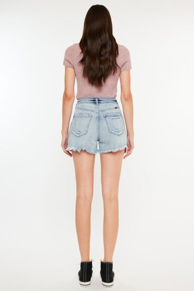 Model from behind showcasing Kancan distressed high-waist denim shorts with pockets and a raw hem.