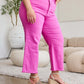 Woman wearing pink high-waisted tummy control raw hem jeans, standing on a carpeted floor with a stylish indoor background.