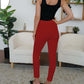 Woman modeling FAM-FAM High Waist Skinny Pants in red, showcasing a chic and stylish look in a modern living room setting.