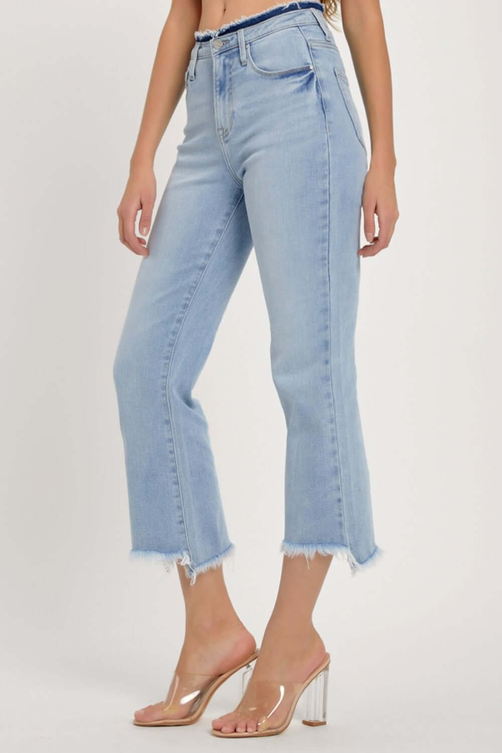 High rise raw edge crop jeans with pockets and slight stretch in light blue denim, paired with clear high heel sandals