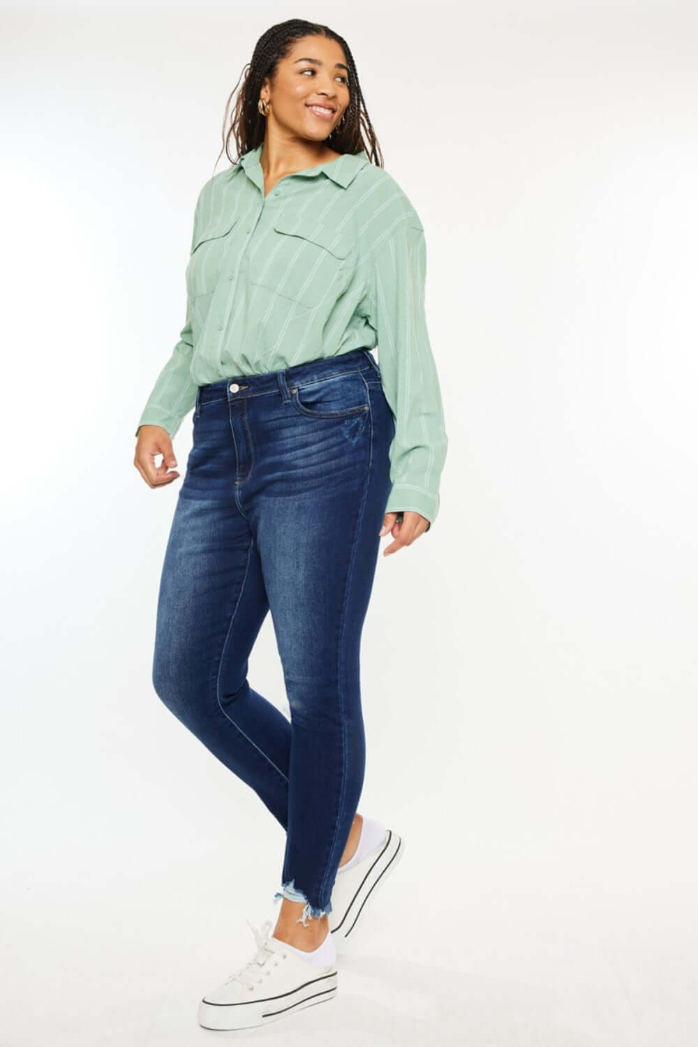 Woman wearing high-rise frayed ankle skinny jeans with a light green shirt and white sneakers, showcasing a trendy casual look.