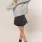 Fashion-forward woman wearing HYFVE distressed cable-knit sweater with a round neck, paired with a black skirt and boots.