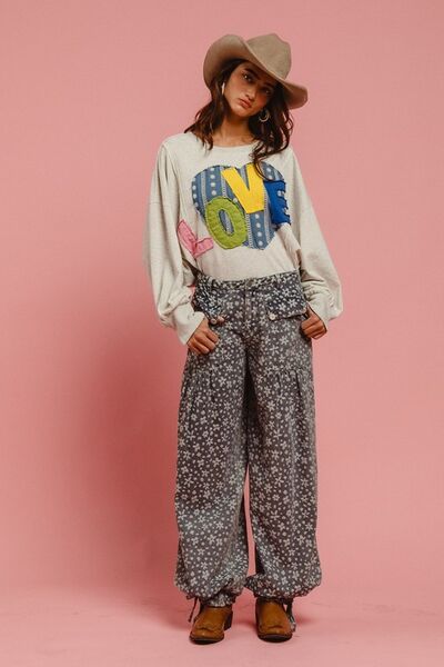 Model wearing BiBi LOVE Heart Patch Slit French Terry Sweatshirt with floral pants against a pink background.