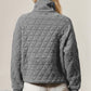 Woman wearing a gray quilted half zip sweatshirt with long sleeves, featuring a cozy pocket design, paired with white shorts, outdoor setting.