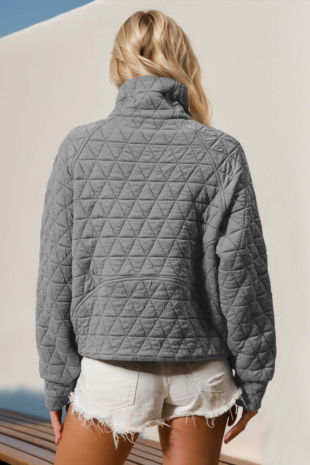 Woman wearing a gray quilted half zip sweatshirt with long sleeves, featuring a cozy pocket design, paired with white shorts, outdoor setting.