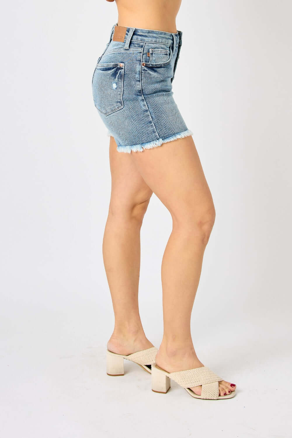 Side view of model wearing Judy Blue Jeans Button Fly Raw Hem Denim Shorts showcasing trendy and stylish summer casual fashion.