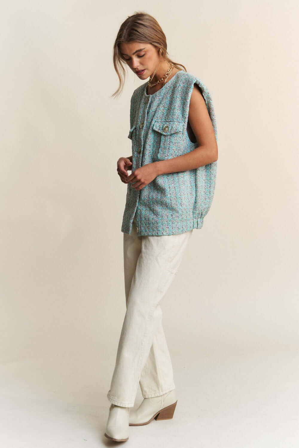 Model wearing J.NNA frayed tweed padded shoulder vest, styled with white pants and boots, showcasing a chic and modern look.