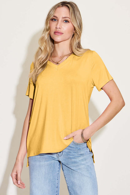 Woman wearing a bamboo V-neck high-low T-shirt in mustard yellow color with slight stretch, paired with jeans.