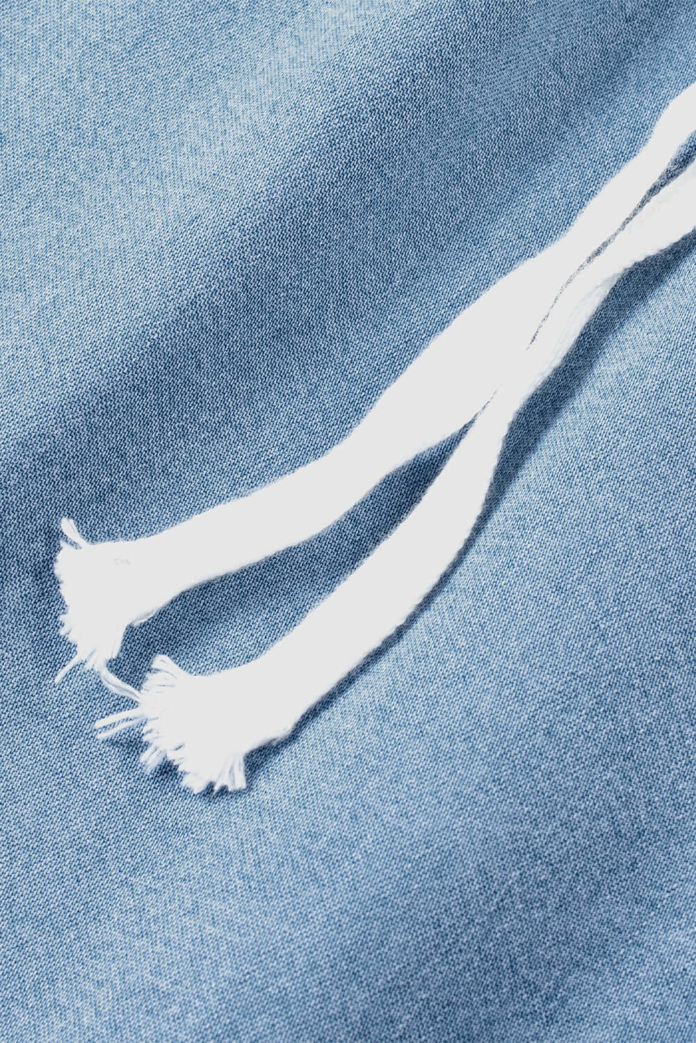 Close-up of white drawstring on light wash denim fabric for stylish cargo pocket jeans.