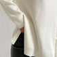 Cozy ivory turtleneck sweater with side slits and dropped shoulders, paired with sleek black pants for a chic look.