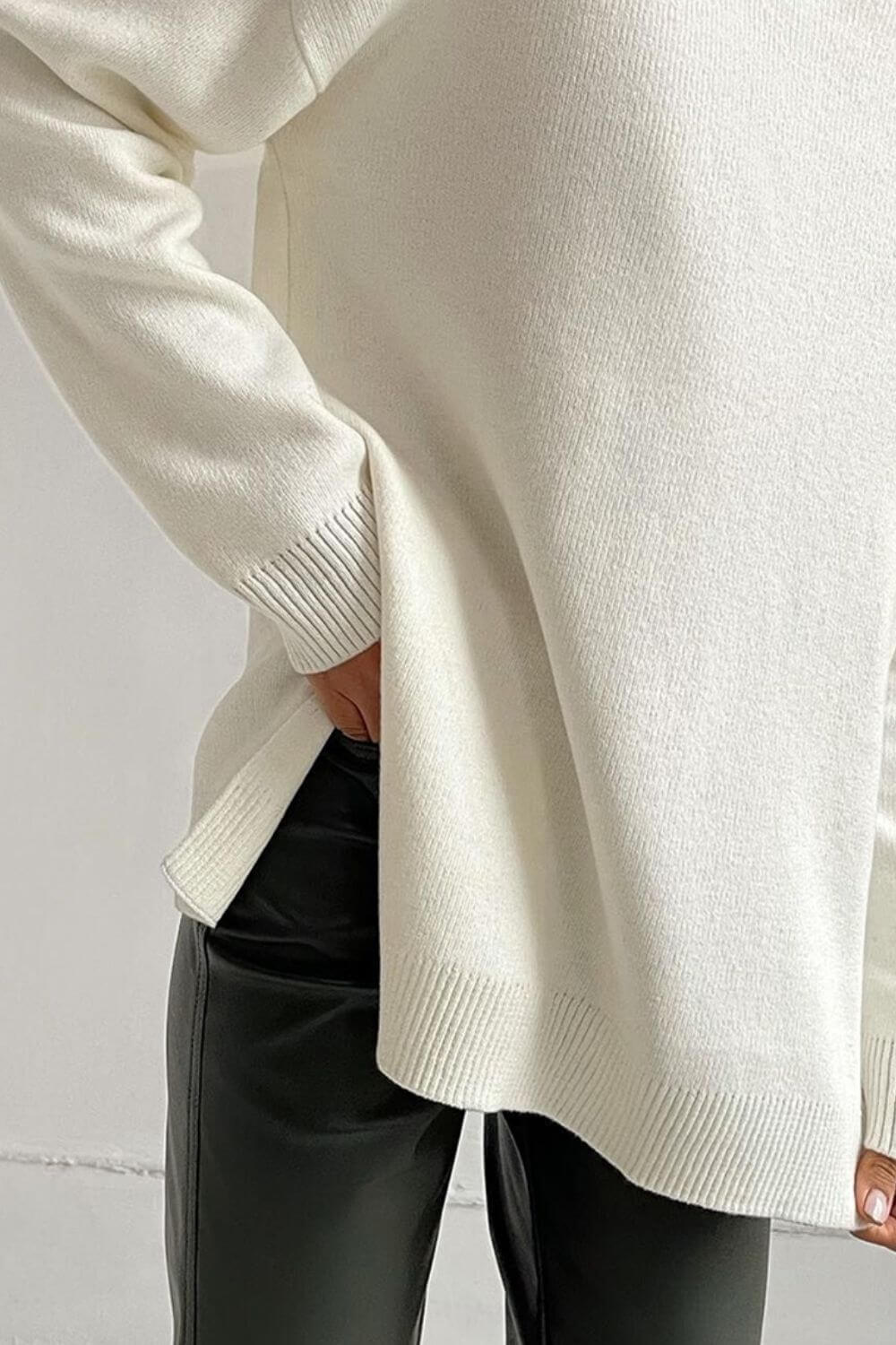 Cozy ivory turtleneck sweater with side slits and dropped shoulders, paired with sleek black pants for a chic look.