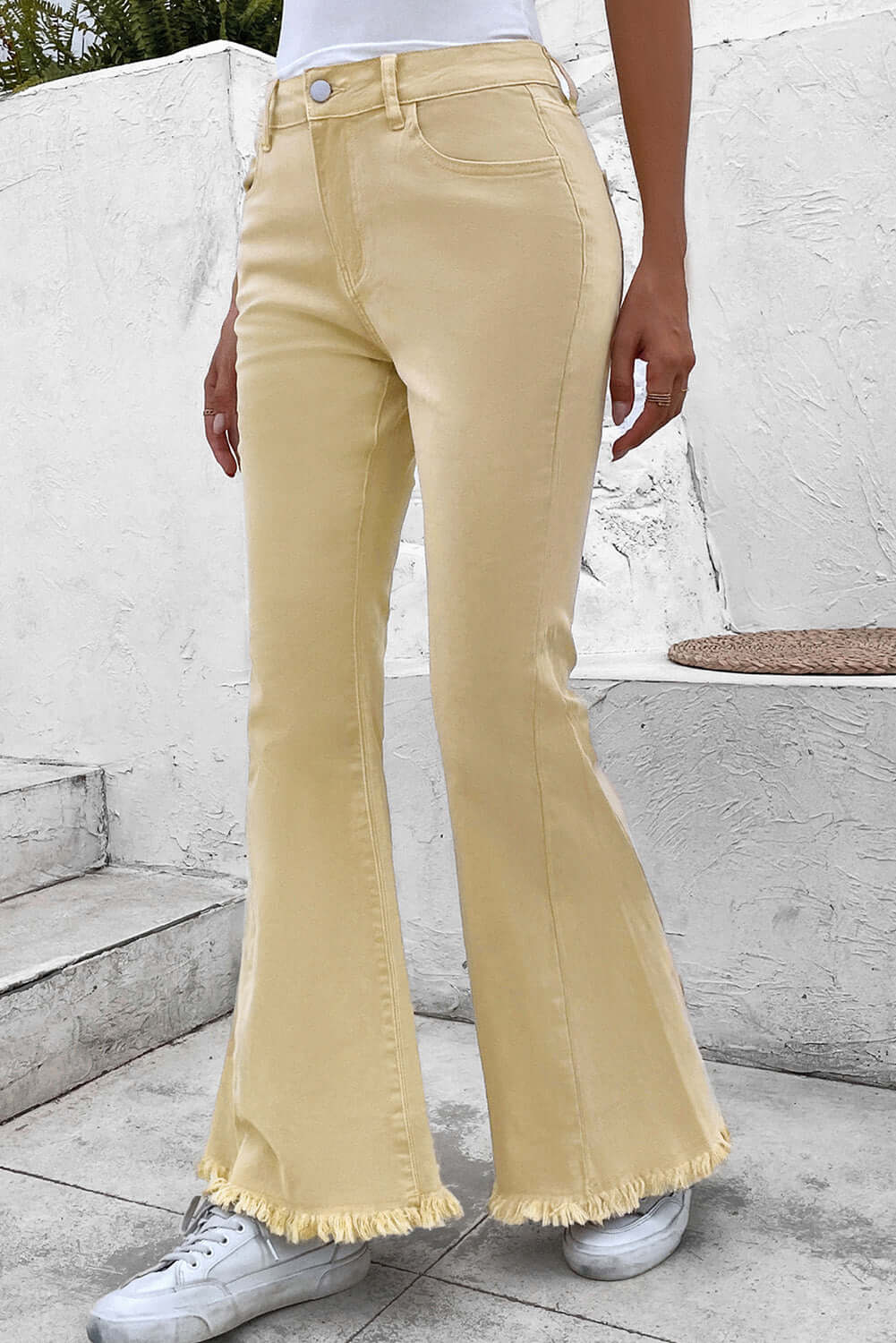 Bella Road Pocketed Raw Hem Flare Jeans in beige with slightly stretchy fabric and a raw hem, styled with white sneakers.