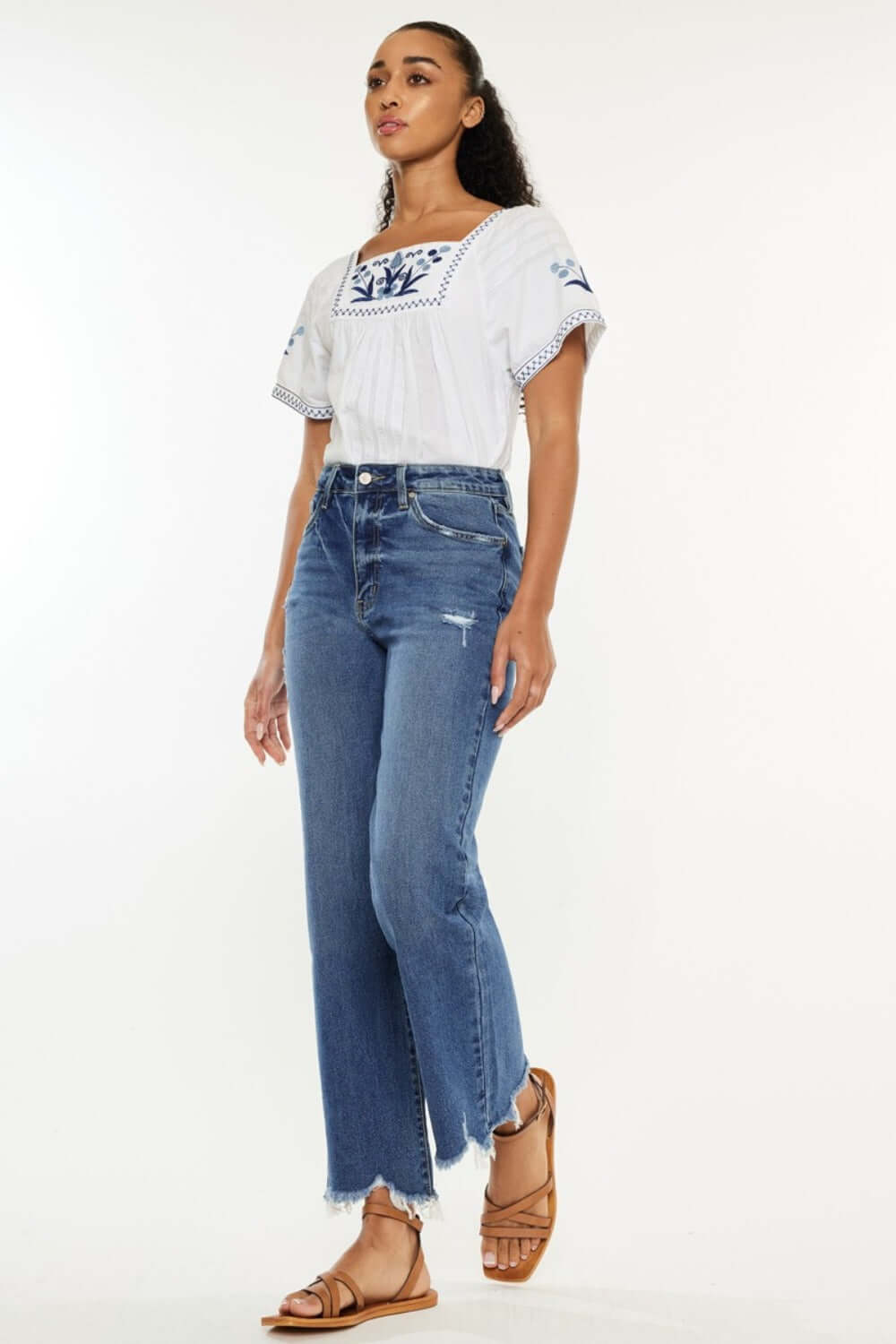 Woman wearing Kancan full size high rise slim wide leg jeans with unique hem, styled with a white embroidered top and sandals.