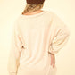 Back view of VERY J Washed V-Neck Exposed Seam Knit Top with drop shoulders, long sleeves, raw edge detail, and exposed seams in beige color.