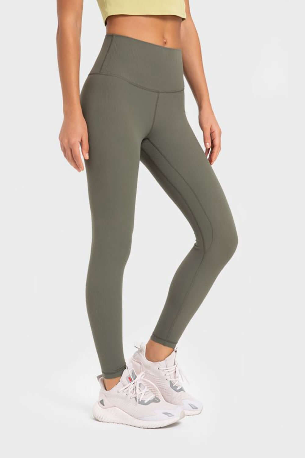 Woman wearing Millennia Highly Stretchy Wide Waistband Yoga Leggings in olive green, paired with white sneakers and a crop top.