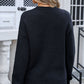 Woman wearing black round neck long sleeve sweater with angel wings bow graphic on the back, paired with denim jeans.