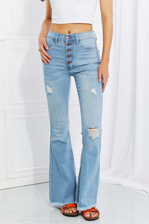 Woman wearing Vibrant MIU Full Size Jess Button Flare Jeans with distressed detailing and frayed hem standing against a white background.