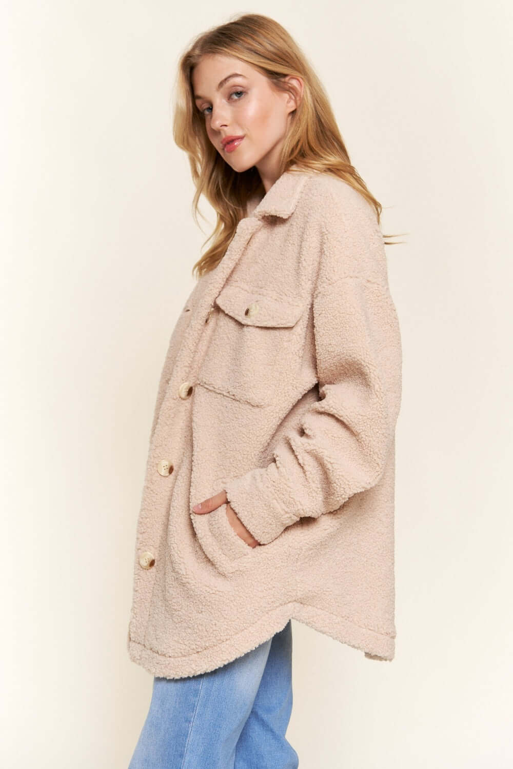 Woman wearing cozy beige teddy sherpa button-down shacket with curved hem, showing stylish layering with relaxed fit and pockets.