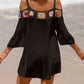 Woman wearing black crochet cold shoulder cover up with three-quarter sleeves and ruffle detail on a beach.