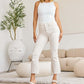 Woman in white tank top and high-waisted raw hem jeans showcasing a stylish outfit in a cozy living room setting.