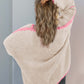 Woman wearing a cozy open front cardigan with contrast pink details, showcasing relaxed dropped shoulder design and wavy blonde hair.