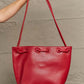 Red vegan leather bucket bag with drawstring closure held by a person against a textured wall.