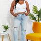 Woman wearing Allie 90's Dad Jean with distressed details, raw hem, and high waist, paired with white crop top, standing in stylish room.