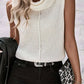 Woman in a white sleeveless turtleneck sweater vest styled with black jeans and a leopard-print clutch.