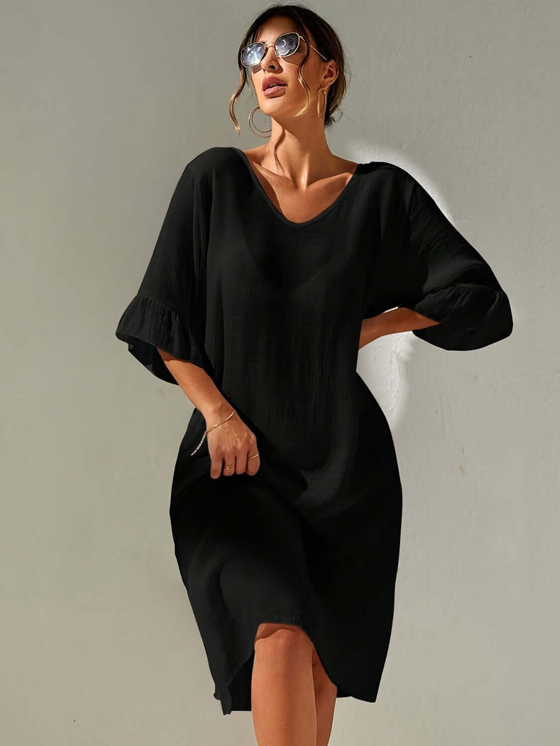 Woman wearing black Slit V-Neck Flounce Sleeve Cover-Up with sunglasses, featuring sheer fabric and backless design