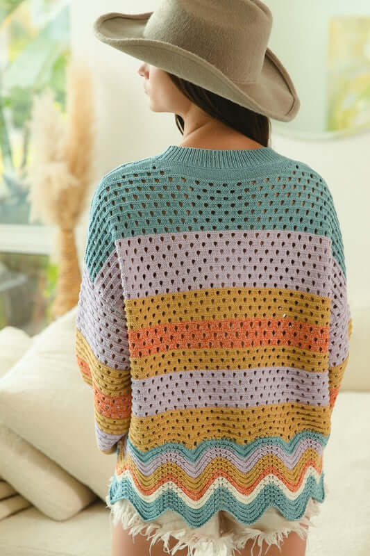 Back view of a woman in a colorful wavy hem openwork sweater and wide-brimmed hat, showcasing its trendy design.