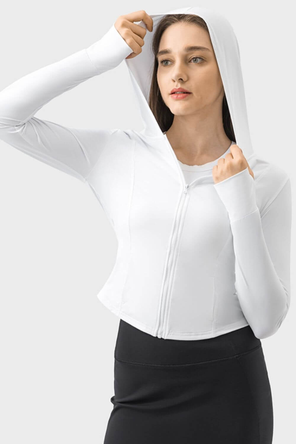 Model in a white zip-up hooded long sleeve active outerwear, showcasing its stylish and comfy design for workouts.