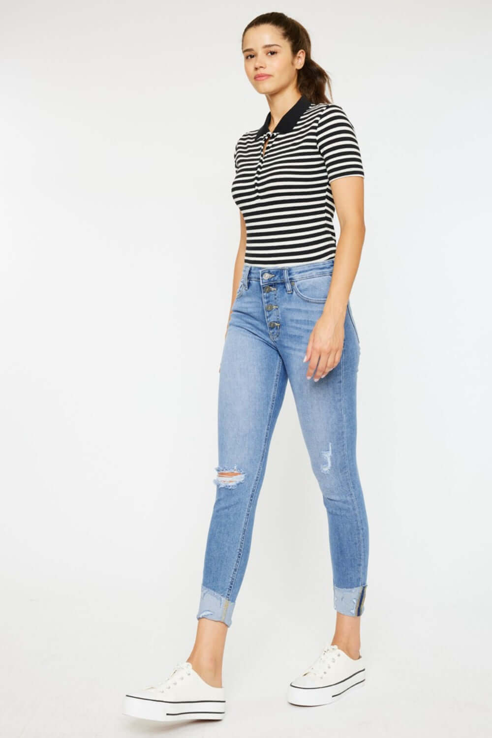 Woman wearing Distressed Cat's Whiskers Button Fly Jeans with a black and white striped top and white sneakers.