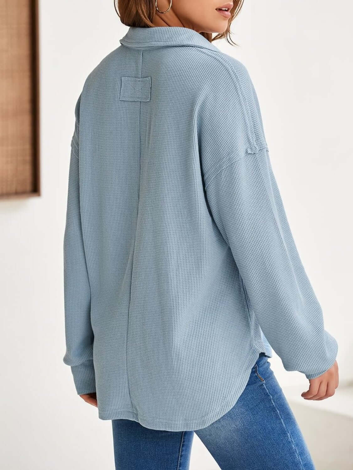 Woman wearing a light blue waffle-knit Johnny collar long sleeve sweatshirt, shown from the back with slightly stretchy material and a casual fit.