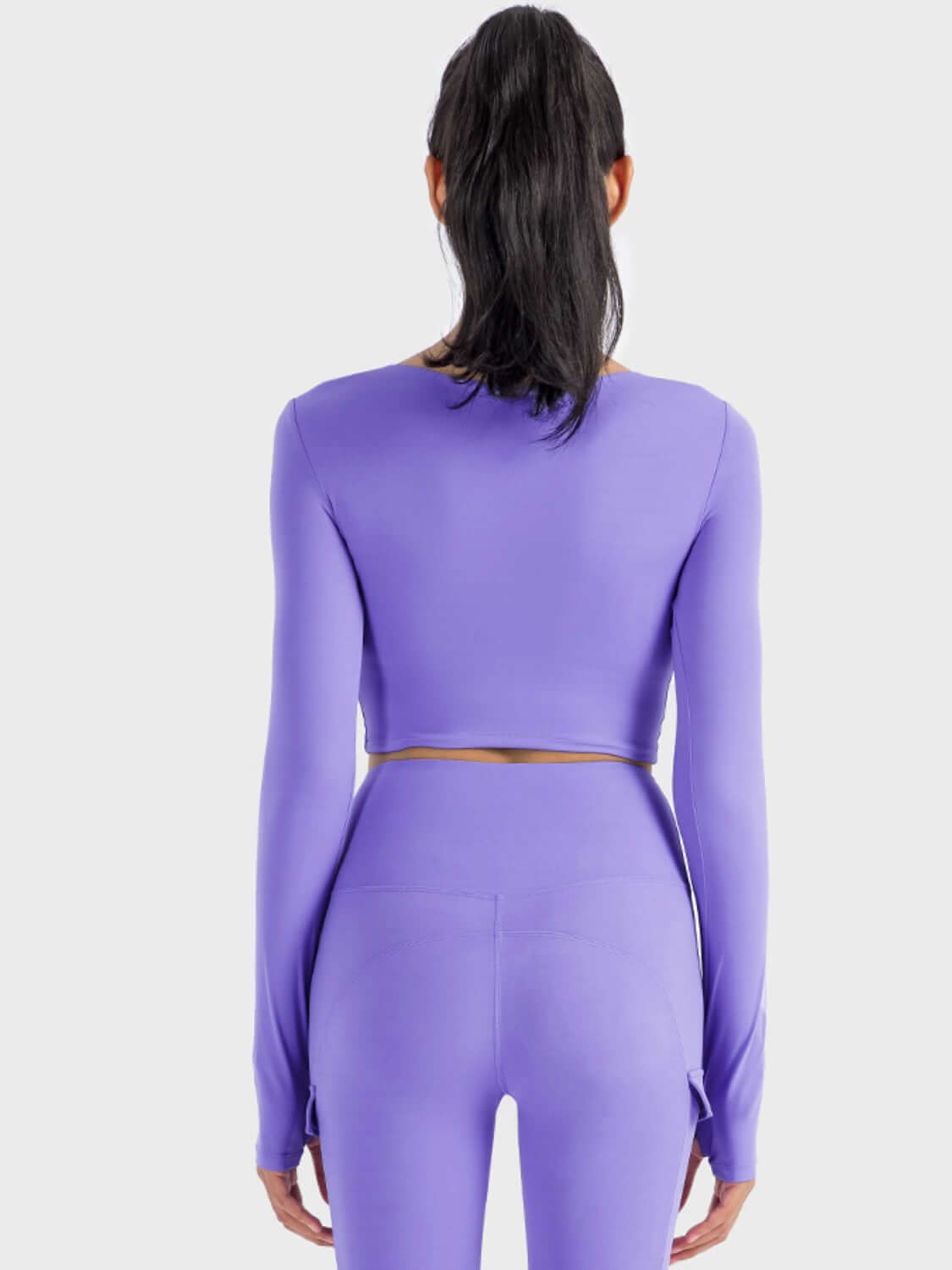 Back view of the Millennia Ruched Cropped Long Sleeve Sports Top in vibrant purple, showcasing its stylish design and fitted look.