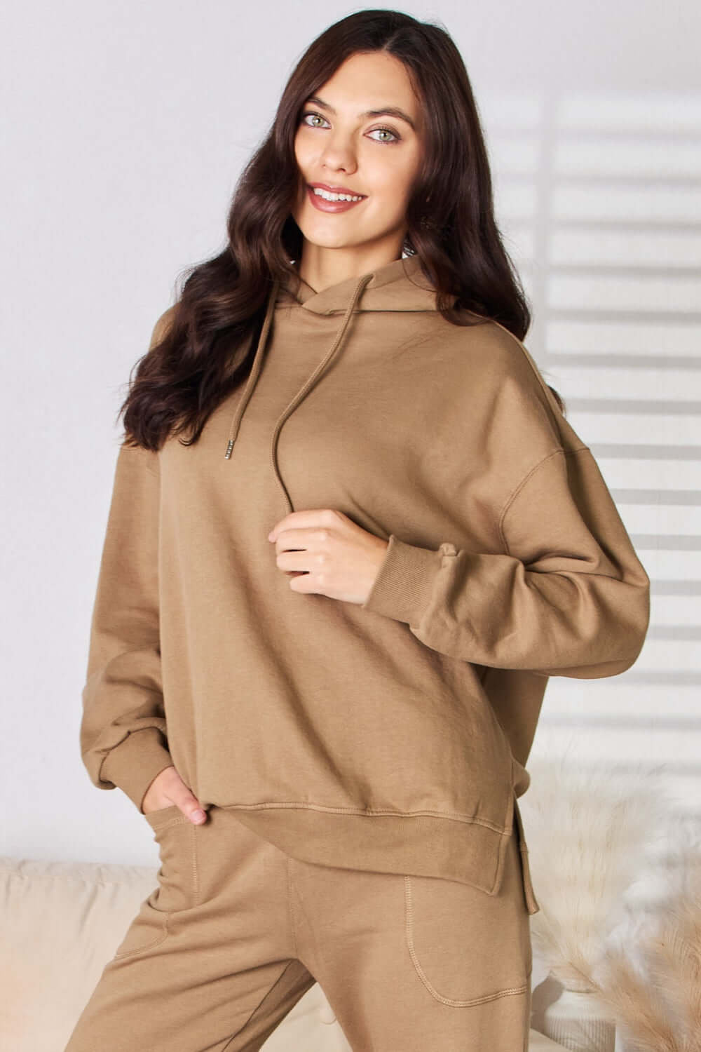 Woman wearing RISEN Drawstring Drop Shoulder Long Sleeve Hoodie in beige, showing casual and comfy style for lounging or casual outings.