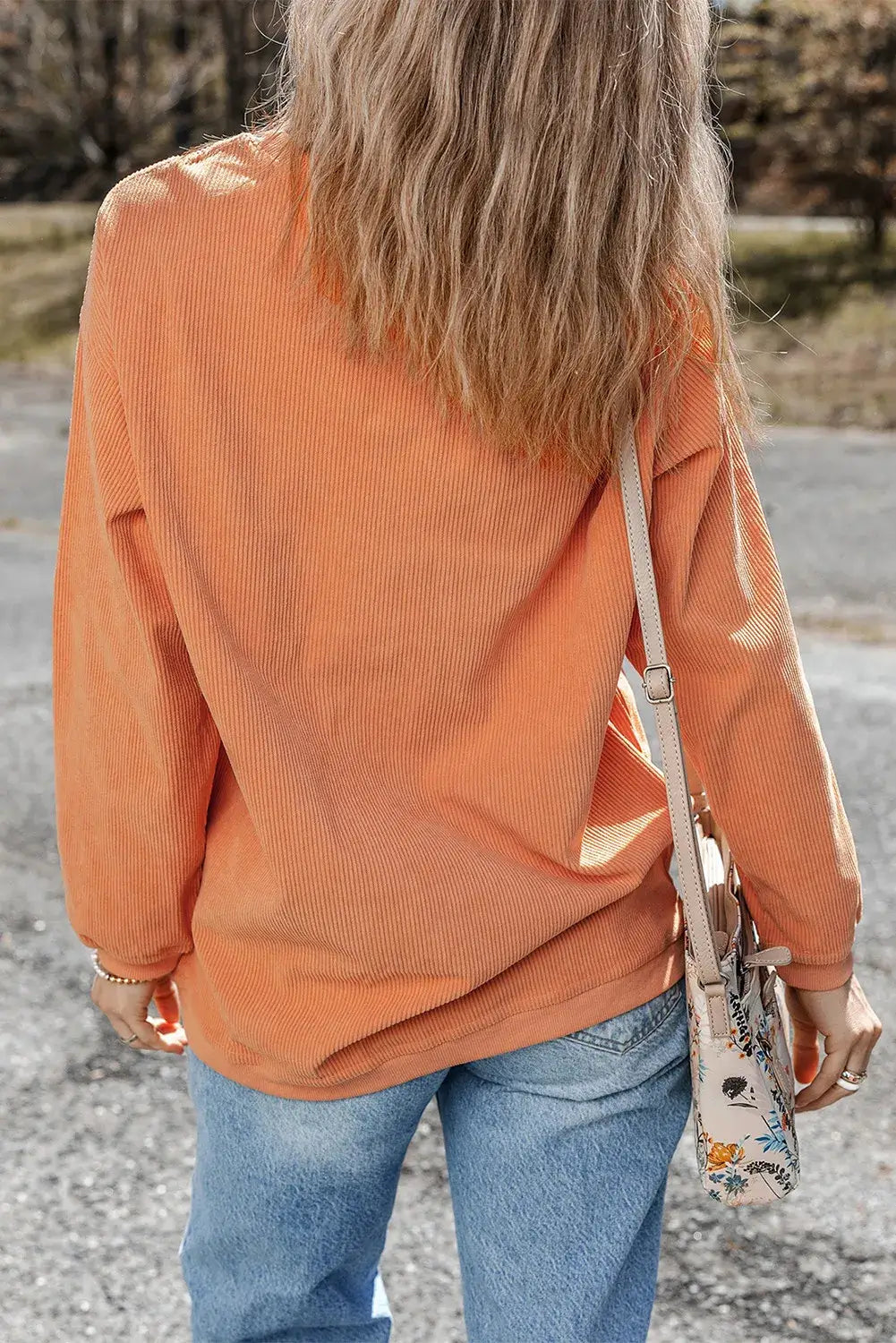 Woman wearing Bella Road THANKFUL Round Neck Long Sleeve Sweatshirt in orange, paired with blue jeans and a floral crossbody bag, standing outdoors.