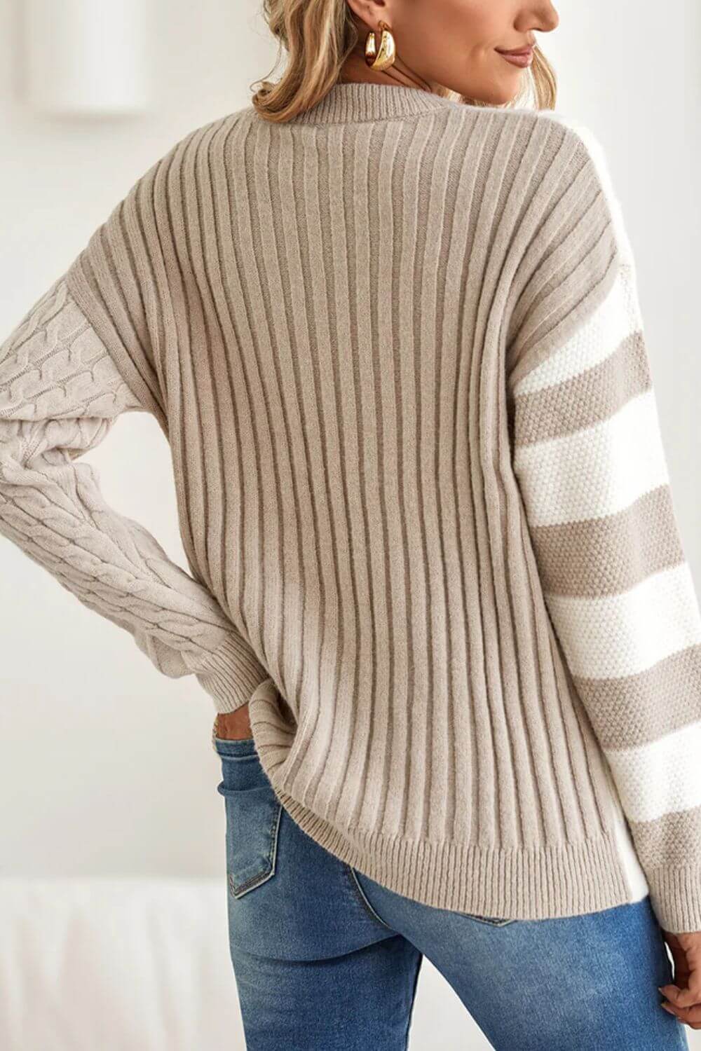 Woman wearing Bella Road tan cable-knit color block round neck sweater with jeans, showcasing cozy fall fashion.