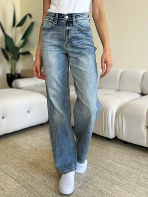 Woman wearing Judy Blue High Waist Straight Jeans standing in living room with white couch and green plants