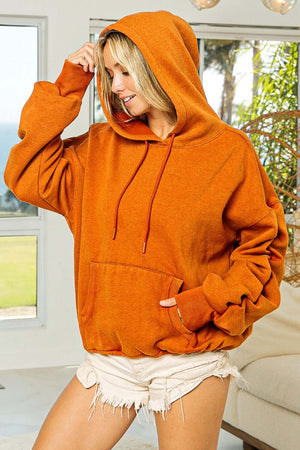 Model wearing a cozy orange ruched long sleeve washed fleece hoodie with pockets and a relaxed fit, perfect for casual outfits.