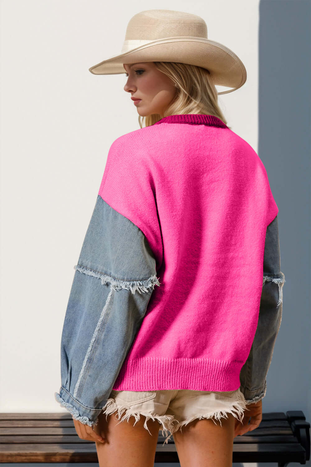 Woman in vibrant pink sweater with denim sleeves and beige hat, standing outdoors.