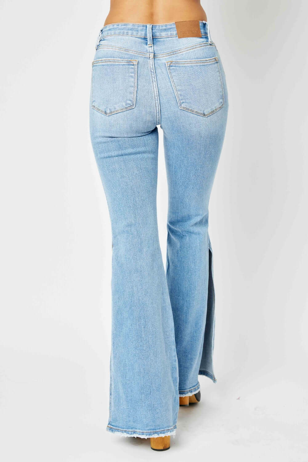 Back view of Judy Blue Jeans Mid Rise Raw Hem Slit Flare in light wash, featuring pocket detail and retro-inspired flare hem.