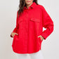 Model in a bold red button-down denim shacket with chest pockets, styled effortlessly with white pants.