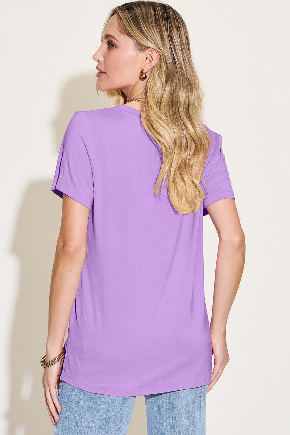 Woman wearing a Bamboo V-Neck High-Low T-Shirt in purple, back view, showcasing slightly stretchy material and basic style.