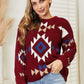 Cozy red sweater with Aztec-inspired pattern, worn by a person, showcasing fuzzy texture and vibrant design.